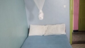 A single bed with a blue mattress and white pillows, a mosquito net hanging above, and a green door to the right. - Four Seasons Lodge (Naivasha)