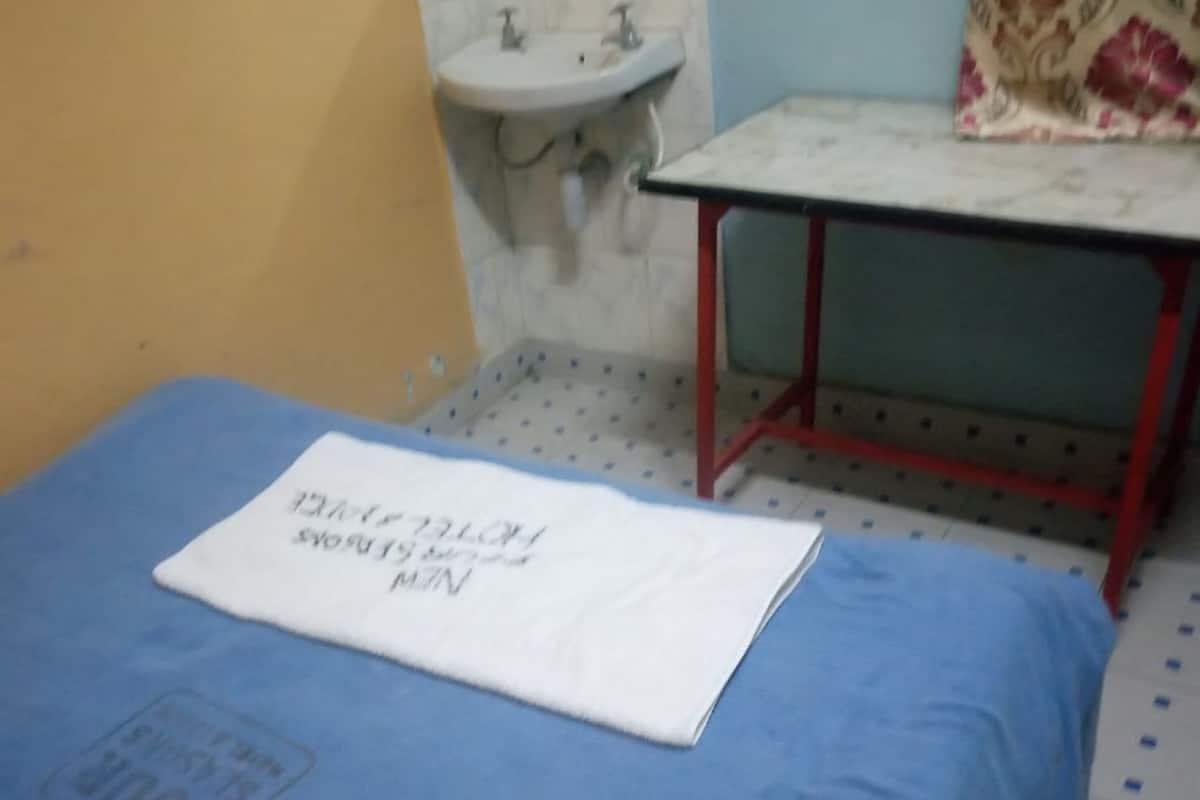 A small room with a single bed, a bedside table, a sink, and a patterned curtain.