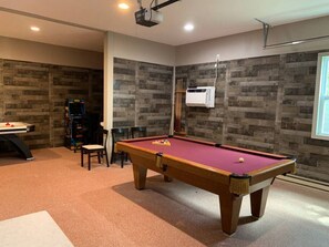 Una mesa de billar en una habitación con pared de madera y un proyector montado en el techo.