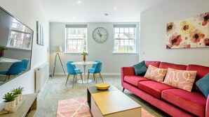 A modern living room with a red sofa, blue chairs, a round table, and a large window. - 2 bedroom accommodation in Mundesley, near North Walsham (Mundesley, near North Walsham)