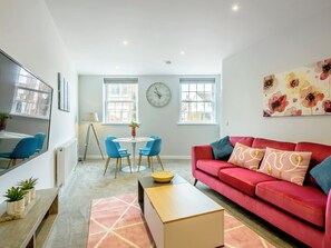 A modern living room with a red sofa, blue chairs, a round table, and a large window. - 2 bedroom accommodation in Mundesley, near North Walsham (Mundesley, near North Walsham)
