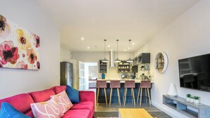 A modern living room with a red sofa, a kitchen with bar stools, and a TV mounted on the wall. - 2 bedroom accommodation in Mundesley, near North Walsham (Mundesley, near North Walsham)