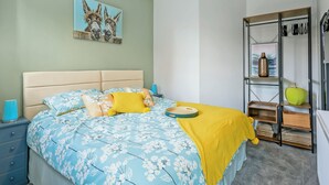 A bedroom with a bed, a nightstand, a dresser, and a shelf with decorative items. - 2 bedroom accommodation in Mundesley, near North Walsham (Mundesley, near North Walsham)