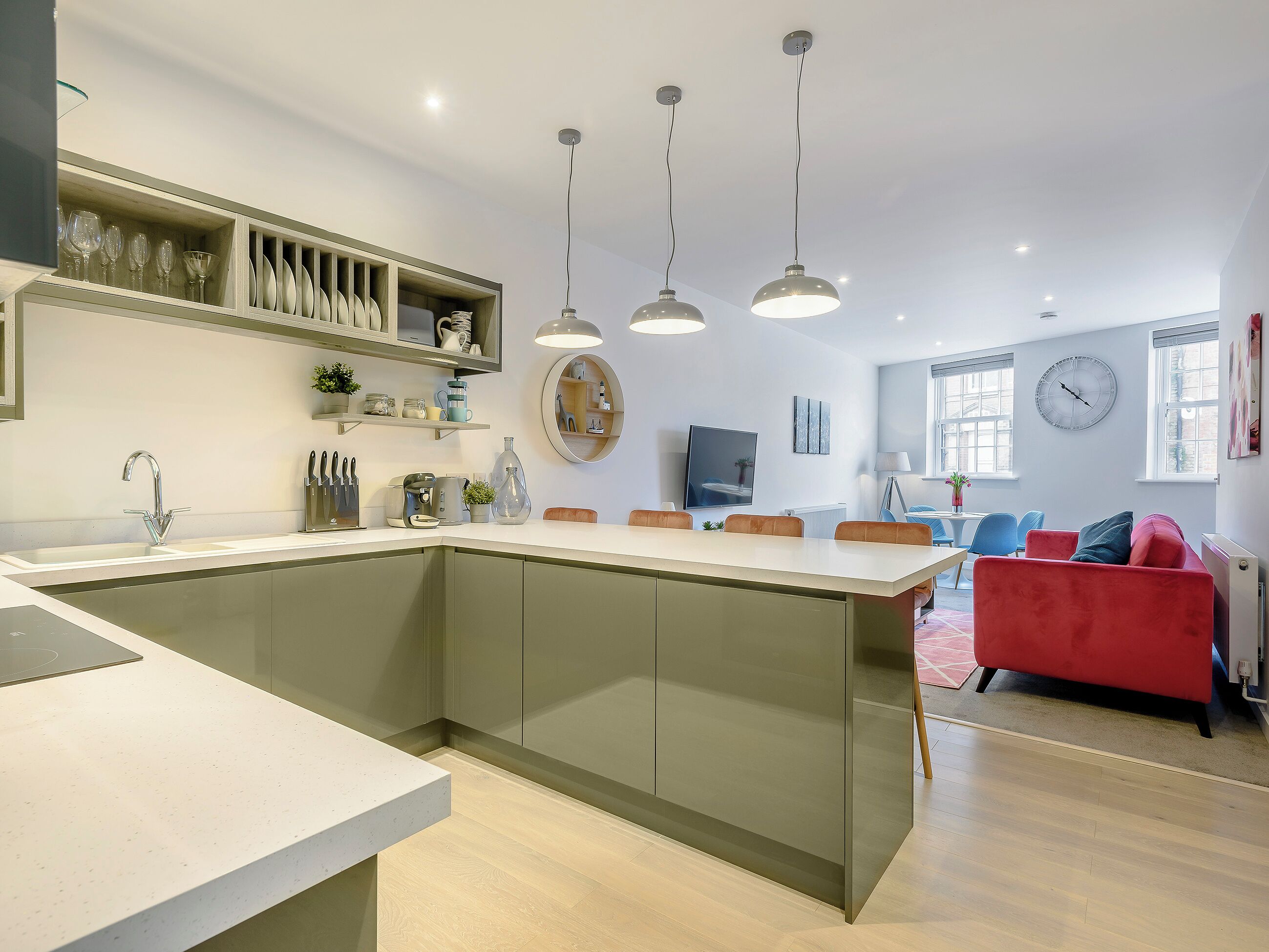 A modern kitchen with a central island, pendant lighting, and a dining area with a red sofa.