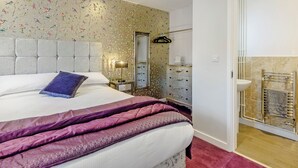 A bedroom with a bed, a dresser, a mirror, and a bathroom with a sink and towel rack. - 2 bedroom accommodation in Mundesley, near North Walsham (Mundesley, near North Walsham)