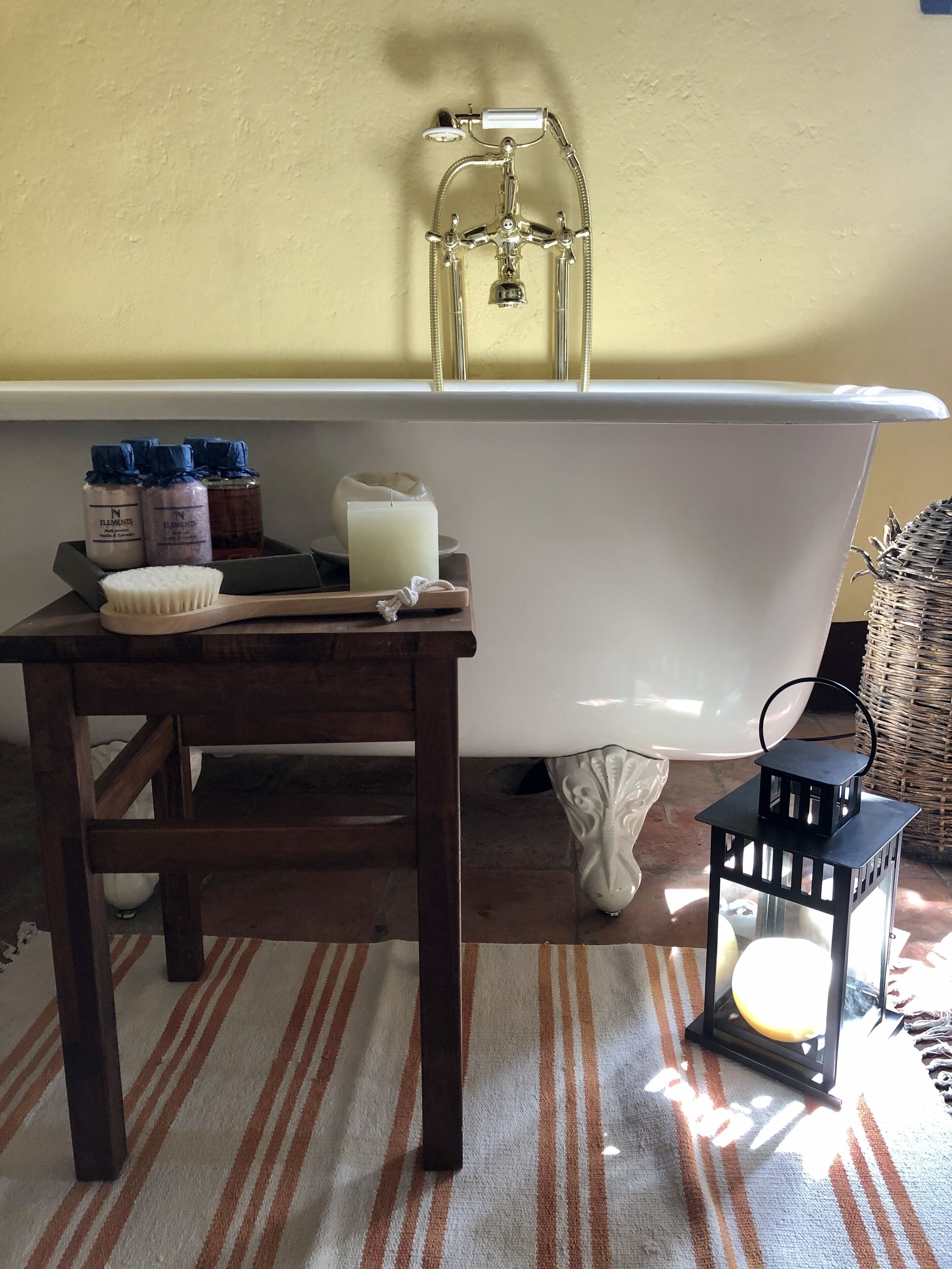 Une salle de bain avec une baignoire, une table en bois sur laquelle sont posés des articles de toilette, une bougie blanche et une lanterne noire.