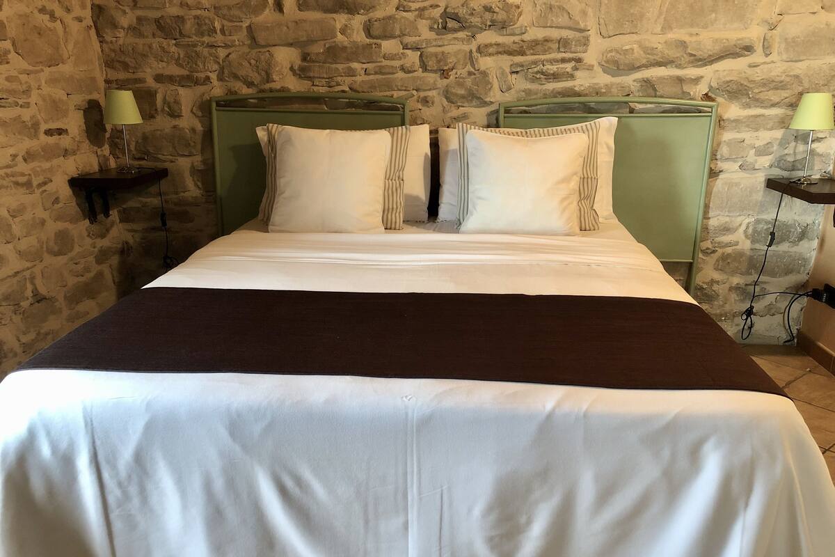 A bed with a white and brown bedspread, two pillows, and a green headboard in a room with a stone wall.