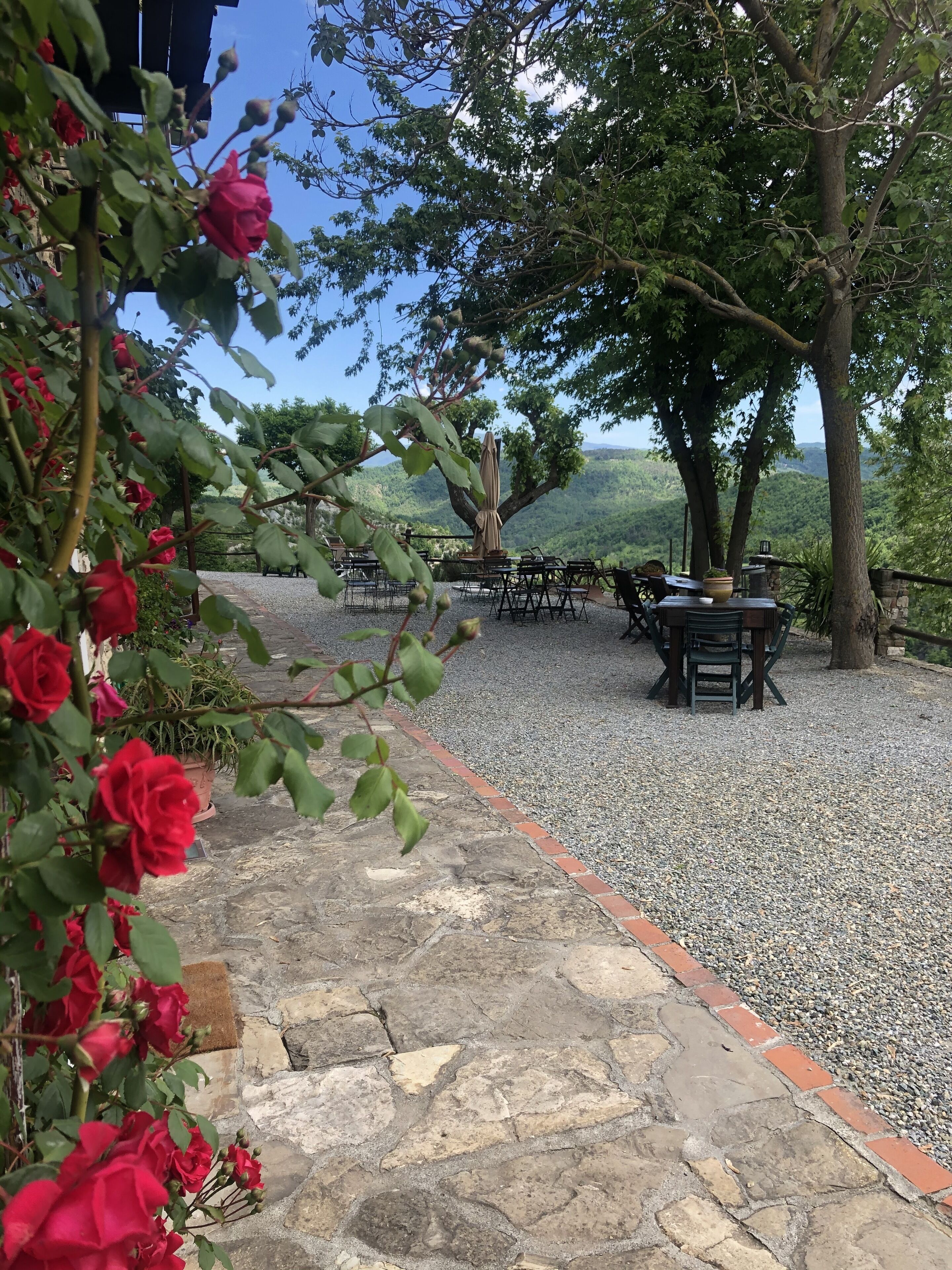 Eine Terrasse mit Steinboden, Gartenmöbeln und Blick auf eine hügelige Landschaft, umgeben von Bäumen.