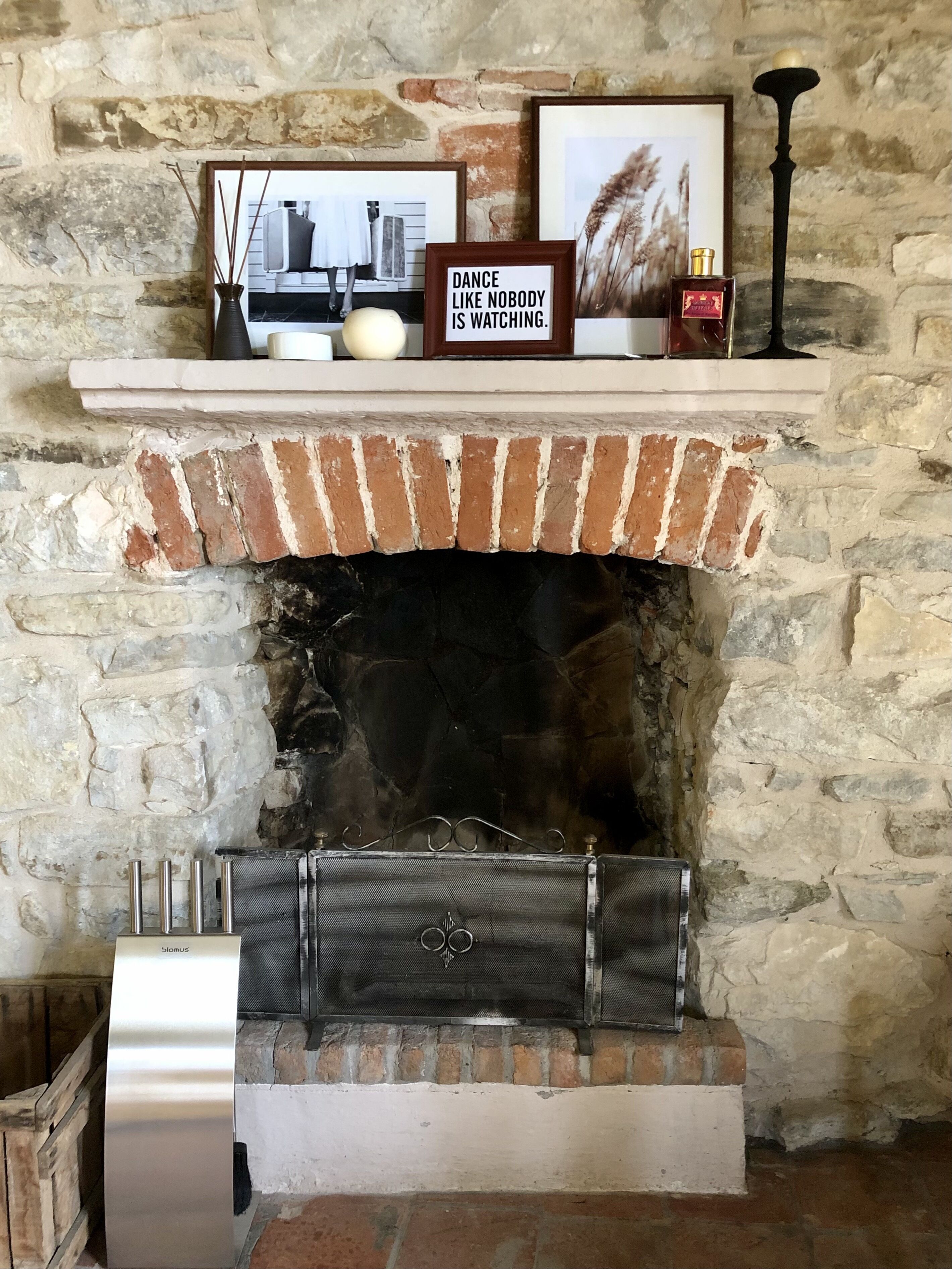 Une cheminée avec un foyer en briques, une étagère ornée d’objets décoratifs et une citation encadrée au-dessus.
