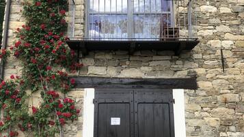 A stone building with a balcony featuring potted plants and a large arched window.