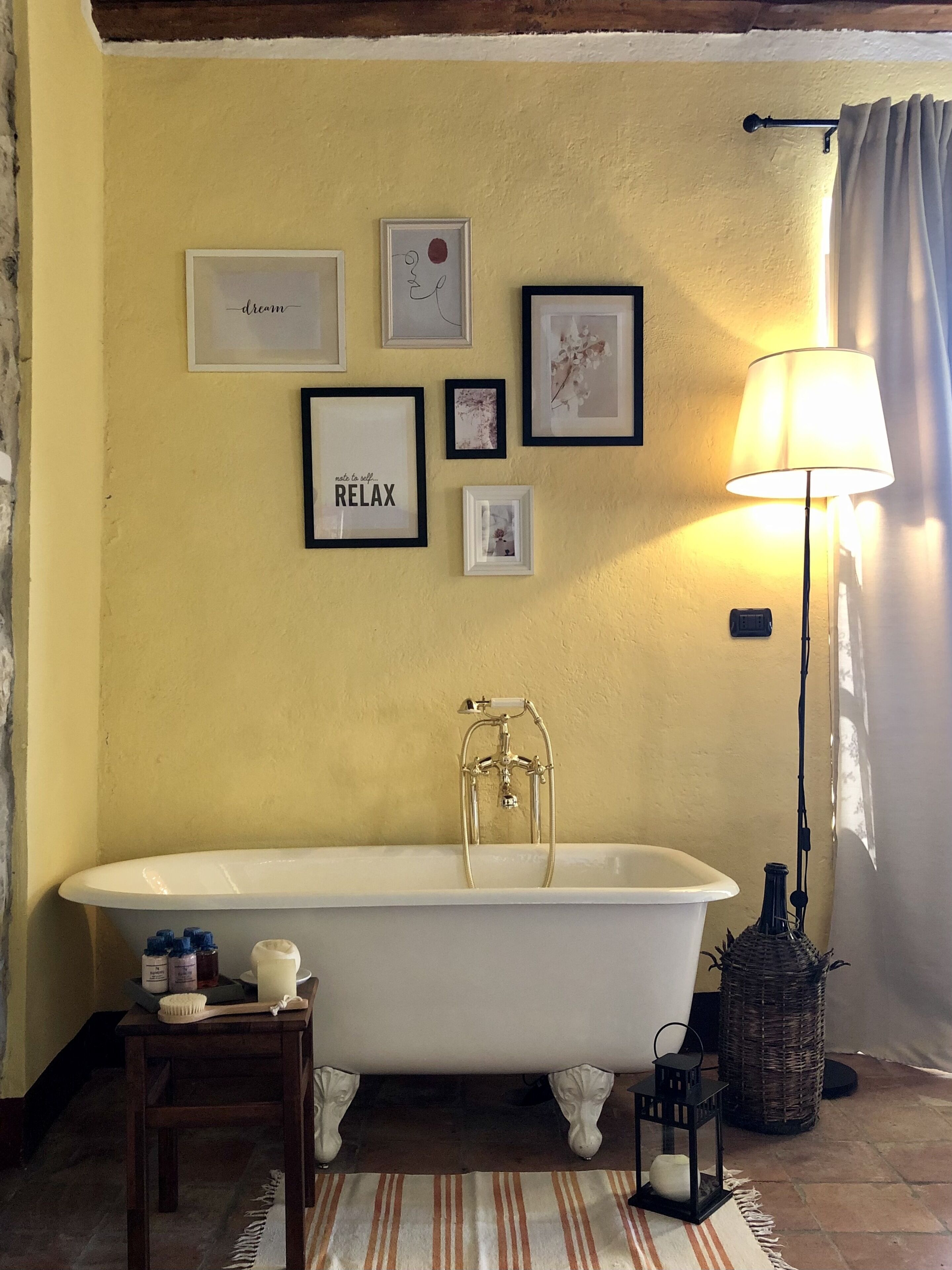 Un baño con una bañera independiente, un taburete de madera, una mesita con artículos de aseo y una lámpara de pie.