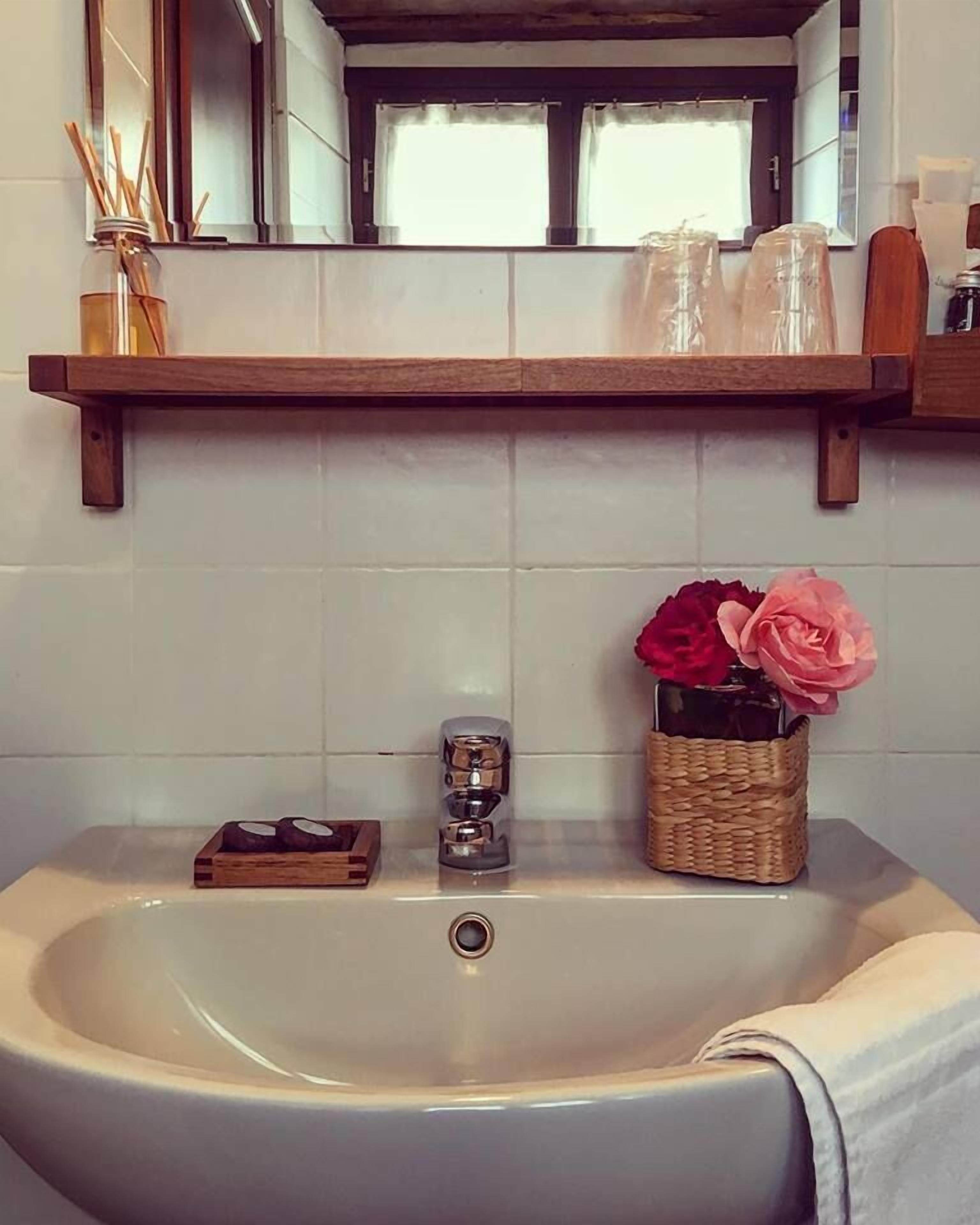 A bathroom with a white sink, a wooden shelf above it, and a mirror.