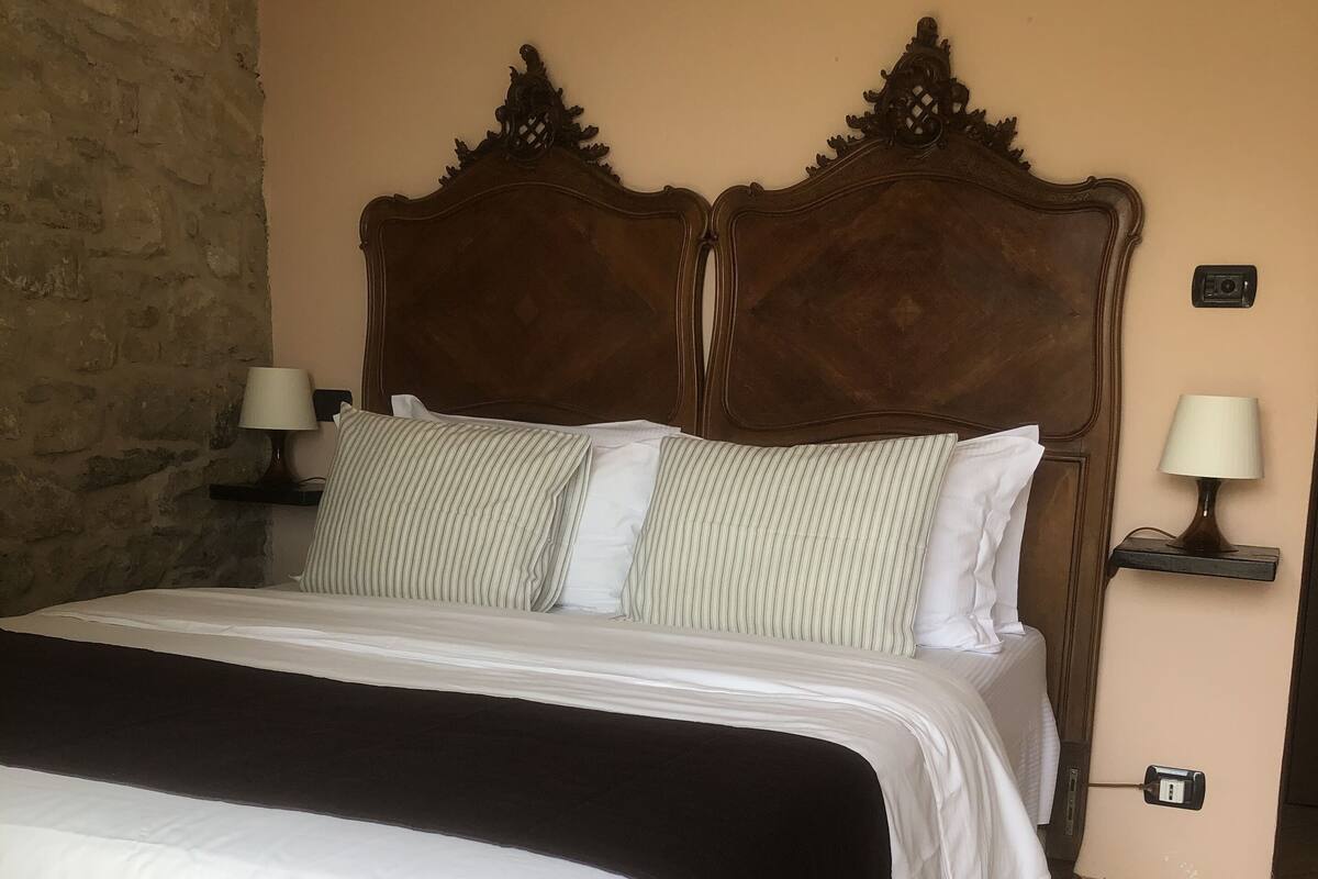 A neatly made bed with a dark headboard, two bedside lamps, and a wall socket.