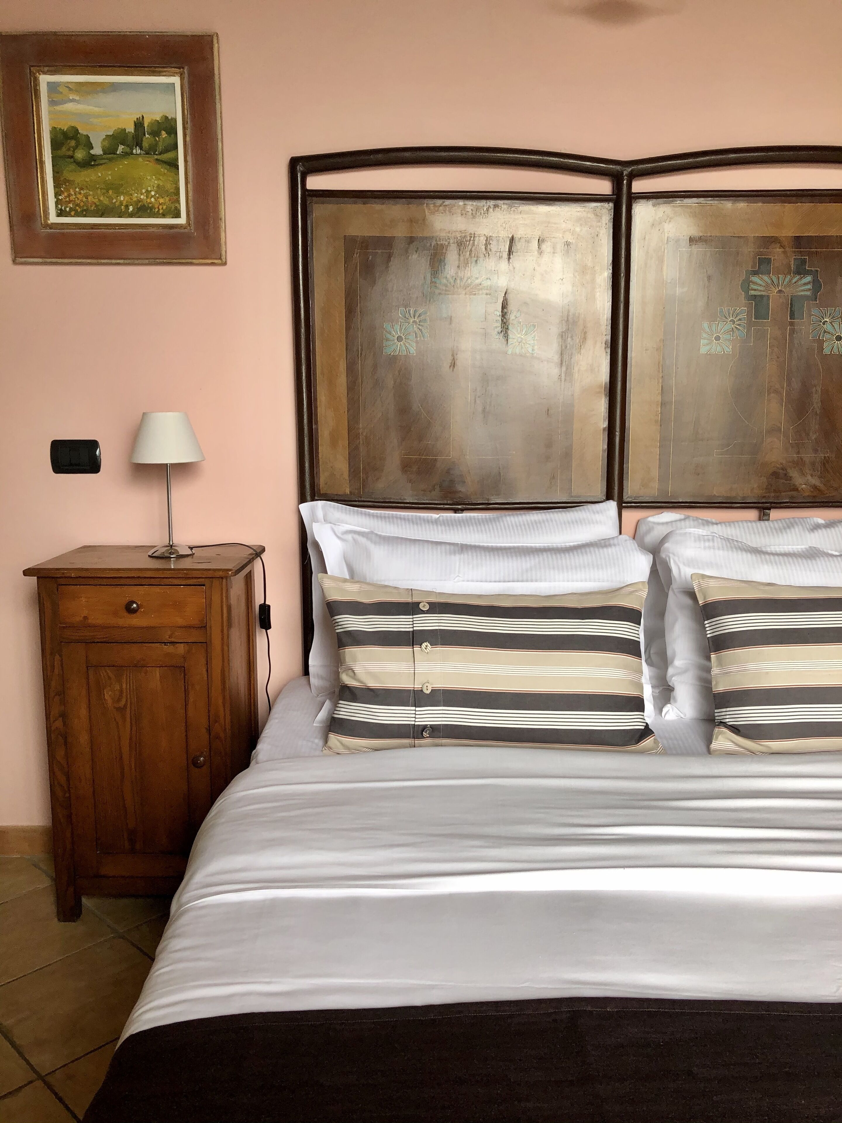 A bedroom with a bed, a wooden nightstand, a lamp, and a framed painting on the wall.