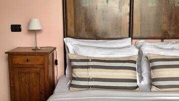A bedroom with a bed, a wooden nightstand, a lamp, and a framed painting on the wall.