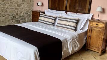 Una cama bien hecha con almohadas a rayas, un plaid negro y un cabecero de madera. Hay dos mesitas de noche con lámparas, una pared de piedra y un cuadro enmarcado en la pared.