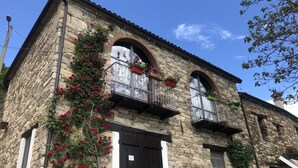 A stone building with arched windows, a balcony with potted plants, and a door. - Cascina Bertolotto Wine Resort. (Spigno Monferrato)
