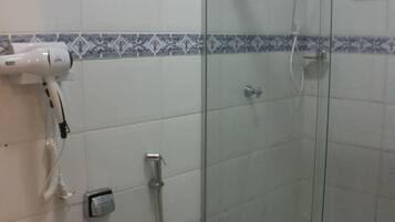 Casa de banho com cabine de duche em vidro, sanita branca e secador de cabelo fixado na parede.