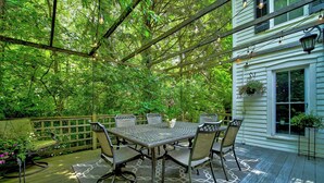 A covered patio with a table and chairs, surrounded by greenery and a wooden fence. -  Tiny House Bungalow (Reynoldsburg)
