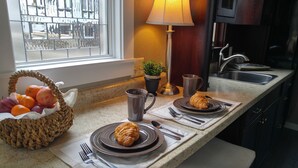 A kitchen counter with a breakfast setup including croissants, a coffee mug, and a fruit basket. -  Tiny House Bungalow (Reynoldsburg)