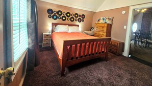 Ein Schlafzimmer mit einem hölzernen Bett, einem Schminktisch, einer Wand voller Schallplatten und einem Fenster mit Jalousien.