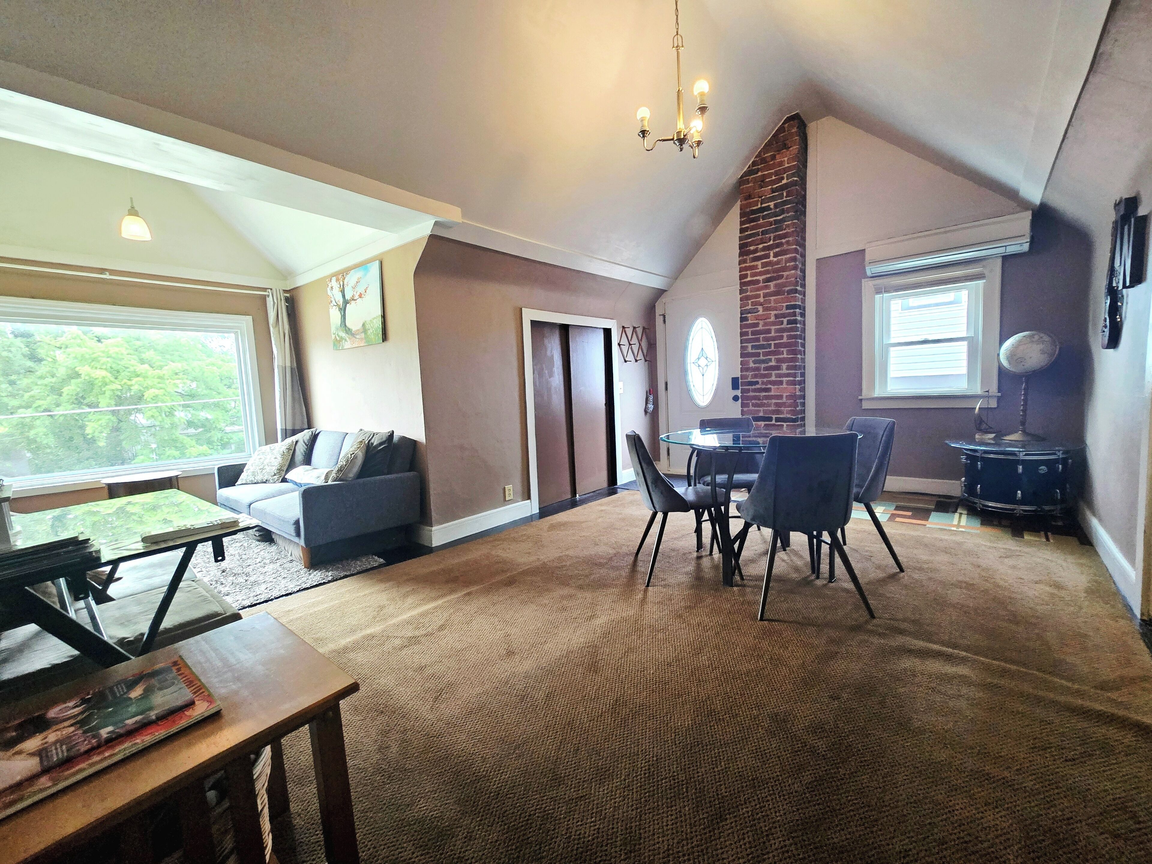 A spacious living room with a high ceiling, a dining area with a glass table, and a view of the outdoors through a large window.
