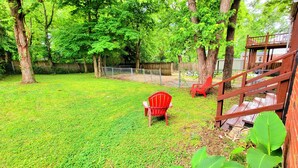 Ein Garten mit Gras, Bäumen, einer Holzterrasse und einem roten Stuhl.