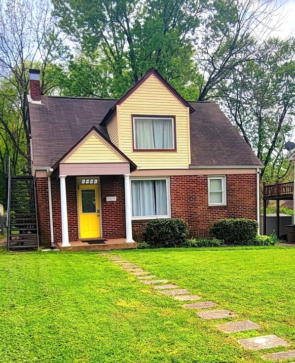 A two-story house with a yellow front door, a brick exterior, and a well-maintained lawn with stepping stones leading to the entrance.