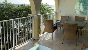 A balcony with a glass table, wicker chairs, and a ceiling fan.