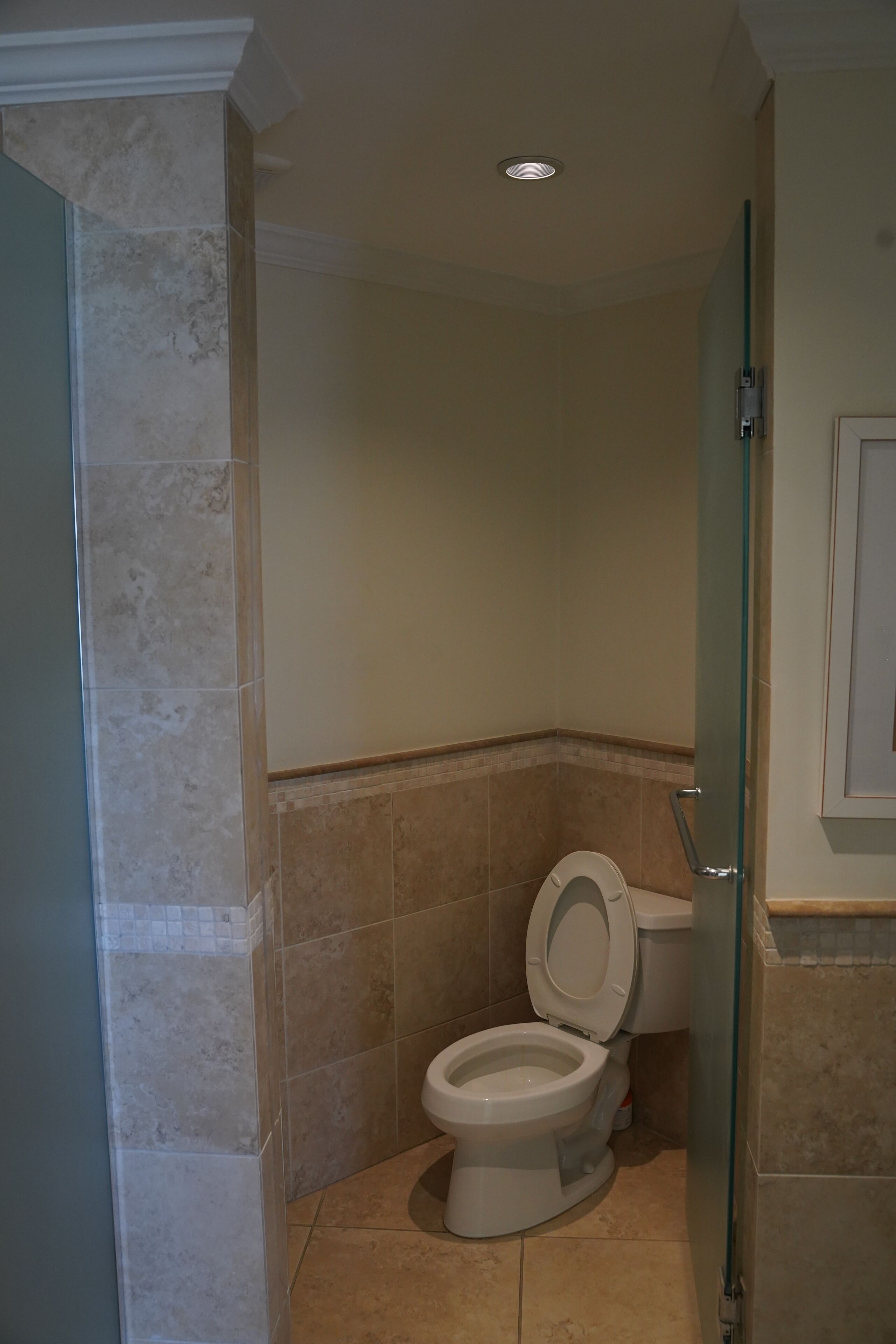 A bathroom with a toilet, a glass shower enclosure, and beige tiled walls.