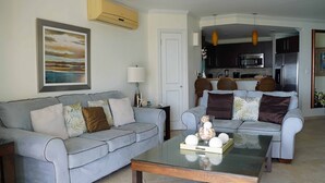 A living room with two grey sofas, a glass coffee table, and a kitchen in the background.