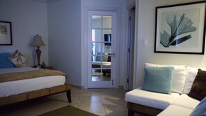 A bedroom with a bed, a bedside table with a lamp, a sofa, and a door leading to a bathroom.