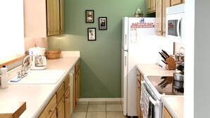 A narrow kitchen with wooden cabinets, a white refrigerator, and a microwave. There are three framed pictures on the wall. - Year Round Green Mountain Escape - Ski - Swim - Tennis - Hike - Golf (Warren)