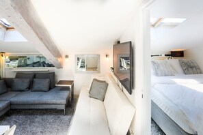 A modern, well-lit room with a sofa, a bed, and a TV mounted on the wall. - 1BR CannesVacationRental by AmericanVacationLiving (Cannes)