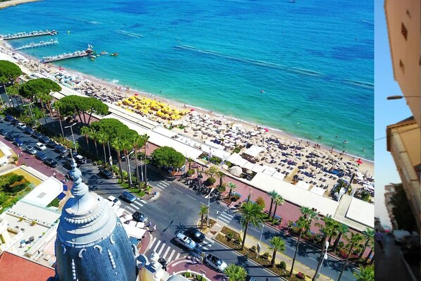 An aerial view of a beach with rows of umbrellas and sun loungers, a clear blue sea, and a prominent building with a dome structure. - 1BR CannesVacationRental by AmericanVacationLiving (Cannes)
