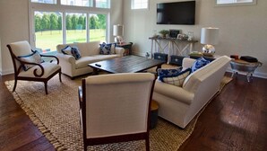 A spacious living room with a large window, a flat-screen TV, and a coffee table.