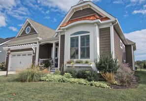 A residential house with a garage, a covered porch, and a well-maintained front yard with various plants.