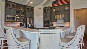 A kitchen with dark cabinets, stainless steel appliances, a central island with bar stools, and an American flag.