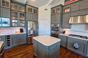 A kitchen with grey cabinets, stainless steel appliances, and a white countertop island.
