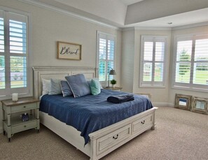 A bedroom with a bed, nightstands, a lamp, and a window with blinds.