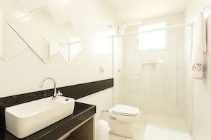 A modern bathroom with a sink, toilet, and glass shower enclosure. - Jurerê Sol & Mar Temporada (Florianópolis)