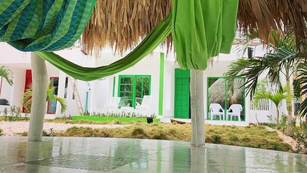 A covered outdoor area with a thatched roof, green and blue checkered fabric, and a green bag hanging. - Bahia Tropical Coveñas (San Antero)
