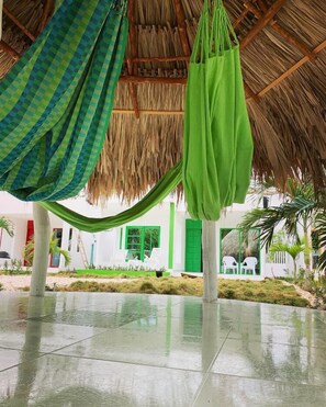 A covered outdoor area with a thatched roof, green and blue checkered fabric, and a green bag hanging. - Bahia Tropical Coveñas (San Antero)