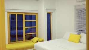 A bedroom with a large bed, a window with yellow blinds, a bench by the window, and a door. - Bahia Tropical Coveñas (San Antero)