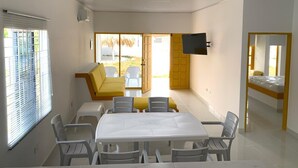 A modern, well-lit room with a dining table, chairs, a sofa, and a TV mounted on the wall. - Bahia Tropical Coveñas (San Antero)