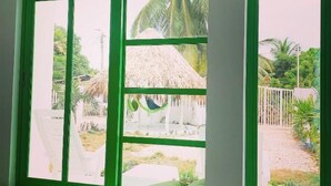 A room with a green window seat overlooking a thatched-roof structure and a garden. - Bahia Tropical Coveñas (San Antero)