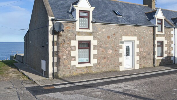 A stone building with a gabled roof, a small porch, and a door with a window above it. - Dolphin View - UK30689 (Portknockie)