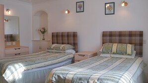 A bedroom with two beds, a dresser, a vanity with a mirror, and wall-mounted lights. - Dolphin View - UK30689 (Portknockie)