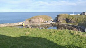 A coastal landscape with a grassy area, a small harbor with boats, and buildings on a cliff. - Dolphin View - UK30689 (Portknockie)