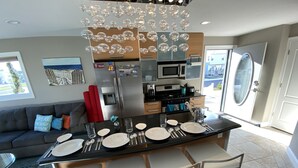 Une cuisine moderne dotée d’un îlot central, d’appareils électroménagers en acier inoxydable et d’un coin repas avec des chaises et une table pour quatre personnes.
